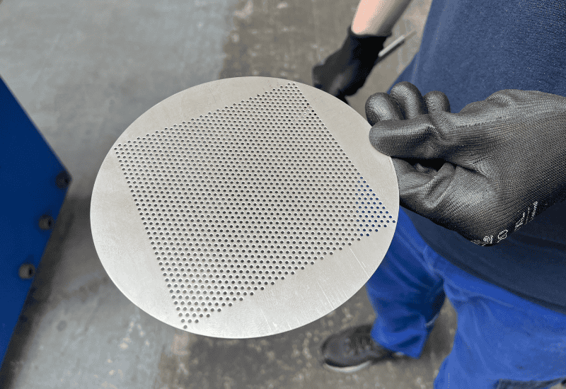 Turn Key Solutions. Perforated Metal Discs A person holding a metal disc with a hole in it.